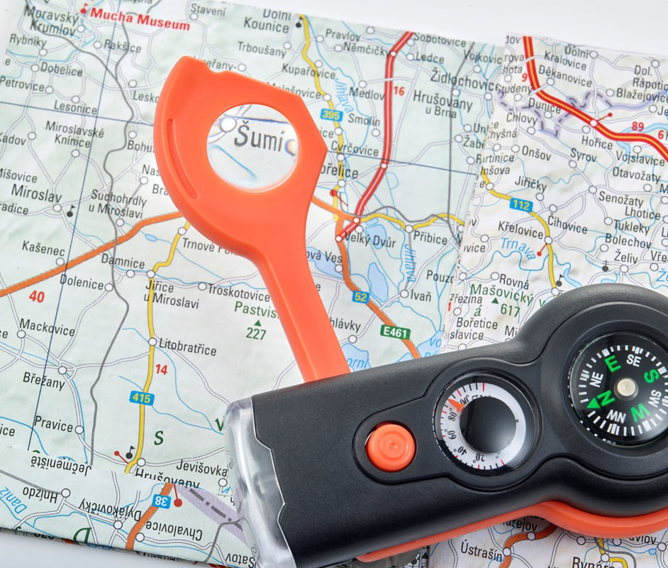 The survival tool being used for its magnifying glass on a map, main body of the tool is black and the sides are orange.