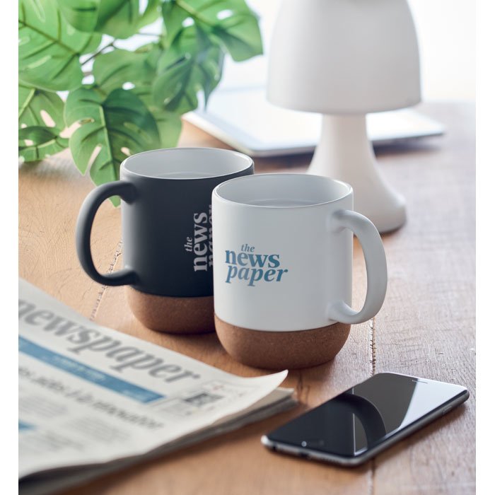 A white ceramic mug, next to a black ceramic mug (both have a light brown cork base)