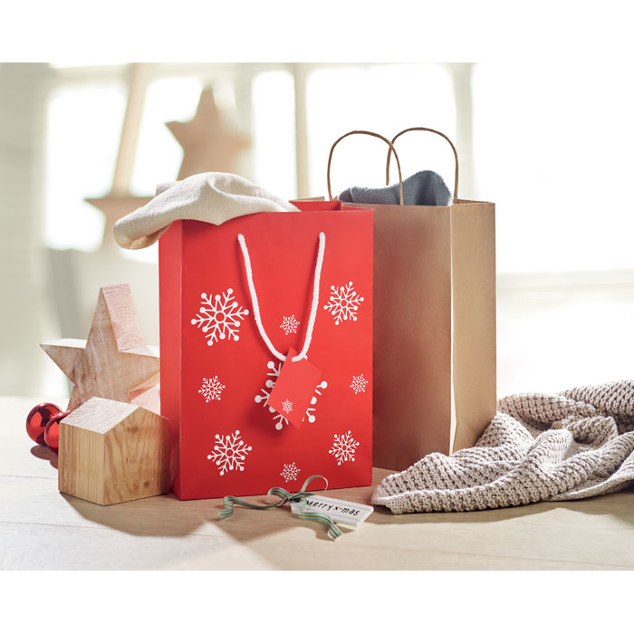 Red paper bag with snowflakes on the front, shown in a display with other christmas bags 