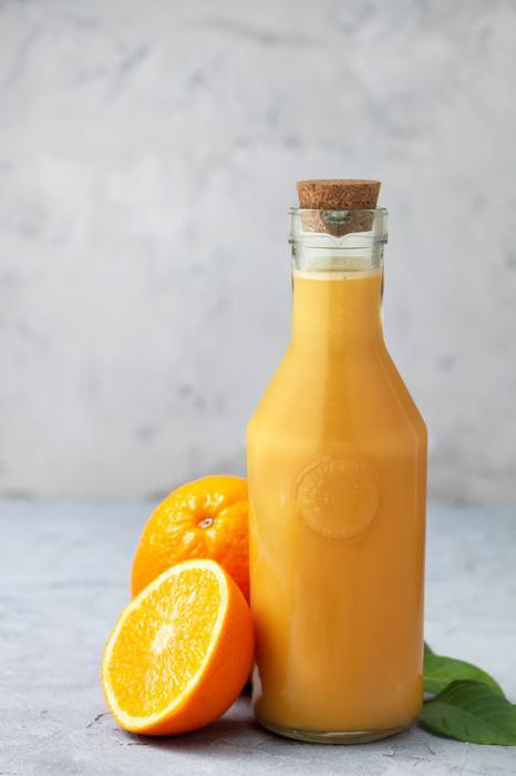 A glass carafe with orange juice inside and an orange to the left of the carafe