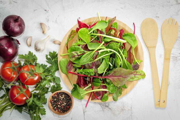 A light brown salad bowl with spoon and fork, on display with salad in the bowl