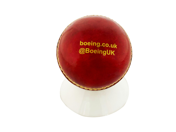 a red cricket ball in a white stand with gold branding 