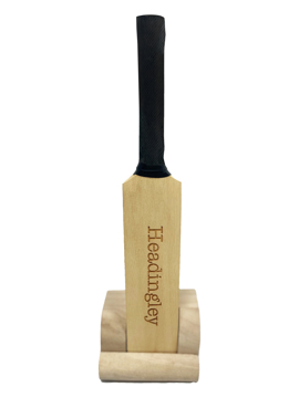 A mini cricket bat, light brown, in a wooden holder 